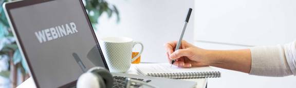 A person attending a webinar and writing on a notepad.