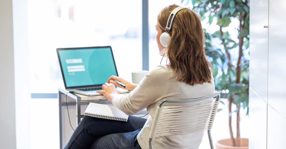 A woman sitting viewing a laptop and wearing earphones.